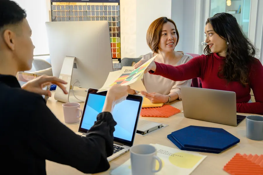 Rekan kerja berdiskusi di meja dengan laptop dan catatan berwarna