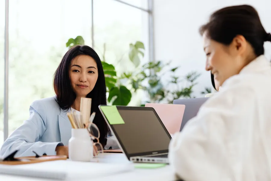Dua perempuan bekerja dengan laptop di kantor yang terang