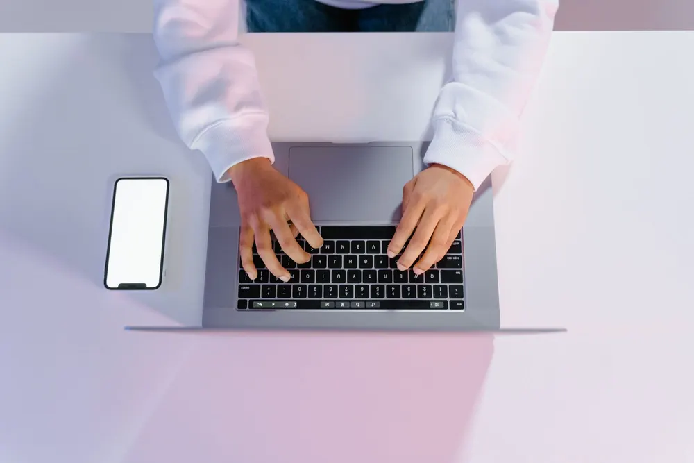Hands typing on a laptop with a phone beside it